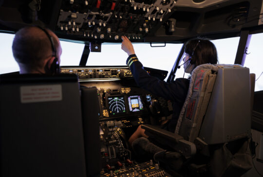 Female pilot assisting captain to takeoff and fly airplane, using buttons on dashboard command in pilot cockpit. Airliners flying plane jet with navigation windscreen and control panel.