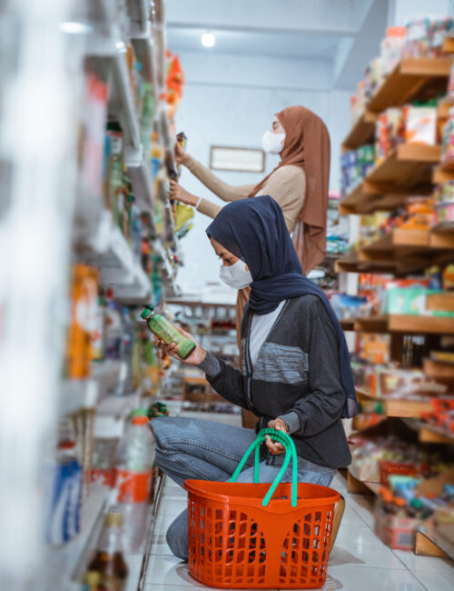 Muslim girl in mask squats carrying a basket while picking up goods at a shop
